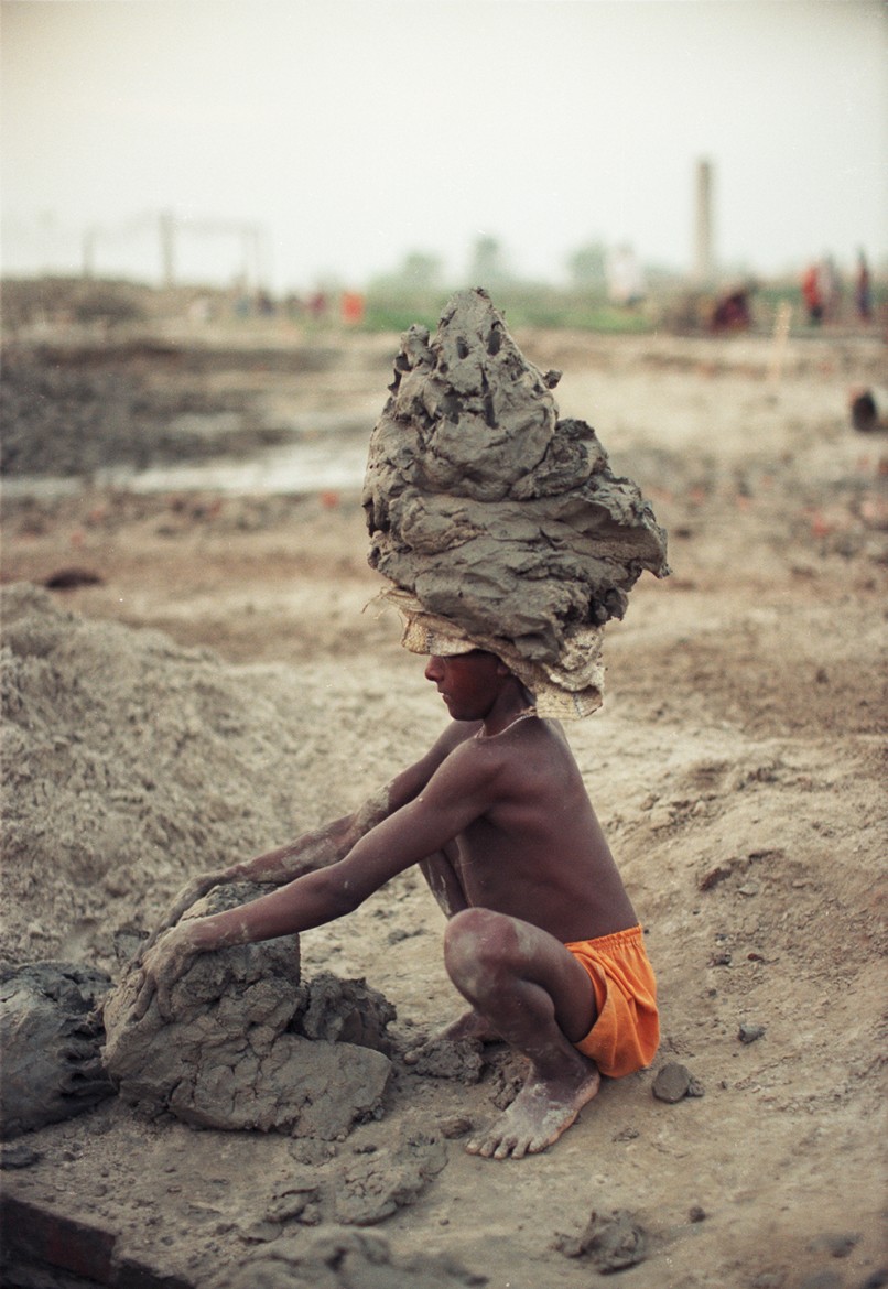 BONDED (SLAVE) CHILD LABOURER LOADING CLAY ON HIS HEAD TO CARRY TO THE DRYING FIELDS.